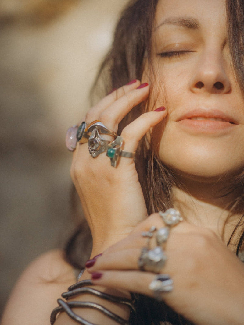 Close-up of a woman's hands with multiple rings and bracelets against a blurred background